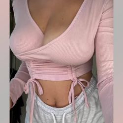 Close-up of a busty social media model with long hair and natural breasts performing hot moves in a pink top and grey shorts.