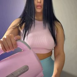 Busty brunette with long black hair in pink crop top and blue shorts pouring water from pink kettle into mug, morning coffee big tits tease