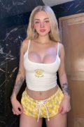 Young blonde independent creator holding the camera for a vertical bathroom video, smiling as she strips off her top to reveal her bouncing perky big breasts.