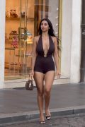 Stylish fashion influencer walking down a bustling city sidewalk during a shopping trip, wearing a low-cut revealing top under natural daylight.