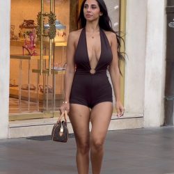 Stylish fashion influencer walking down a bustling city sidewalk during a shopping trip, wearing a low-cut revealing top under natural daylight.