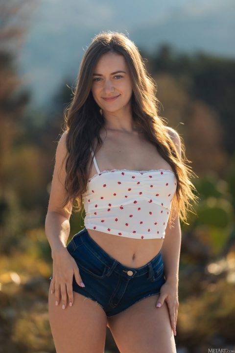 Audrey Sterling smiling in strawberry crop top and tight denim shorts outdoors