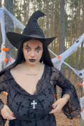Brunette witch in black hat pulling sheer top down to show huge naked breasts in forest