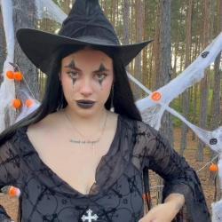 Brunette witch in black hat pulling sheer top down to show huge naked breasts in forest